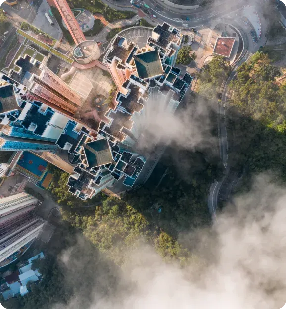 Aerial view of a complex of tall residential buildings partially covered by mist with surrounding trees and roads.