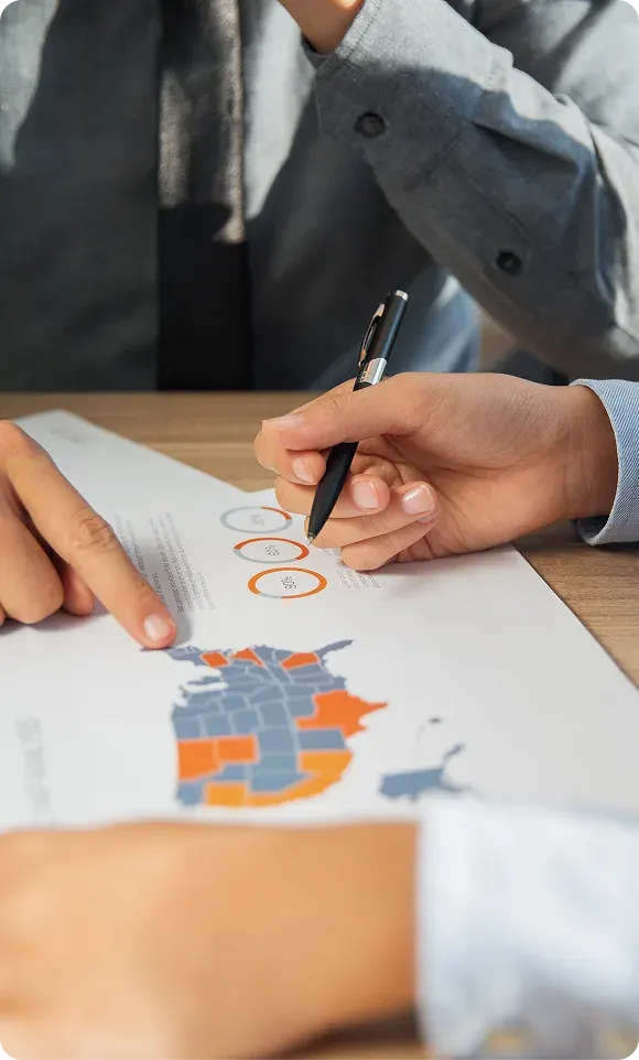 Close-up of hands pointing and writing with a pen on a paper showing a map of Canada with some provinces highlighted in orange and blue.