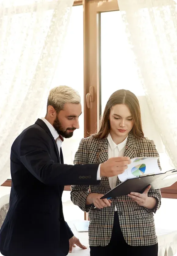 Man and woman in business attire reviewing documents with charts in a bright office setting.