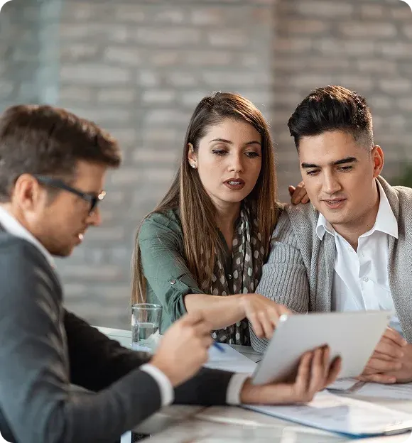 Three professionals reviewing documents on a tablet during a meeting in an office with a brick wall background.