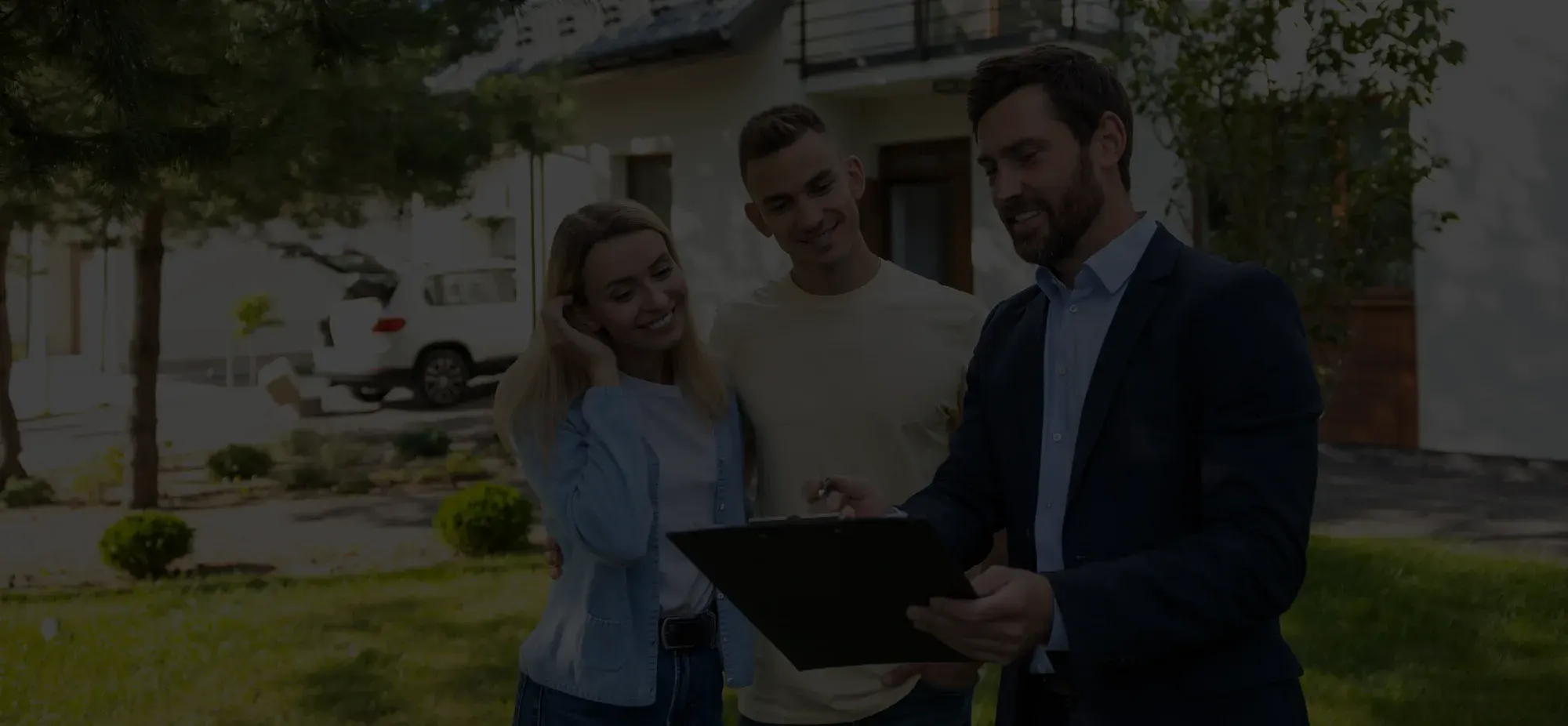 Real estate agent showing a clipboard and discussing with a smiling couple standing outside a house.