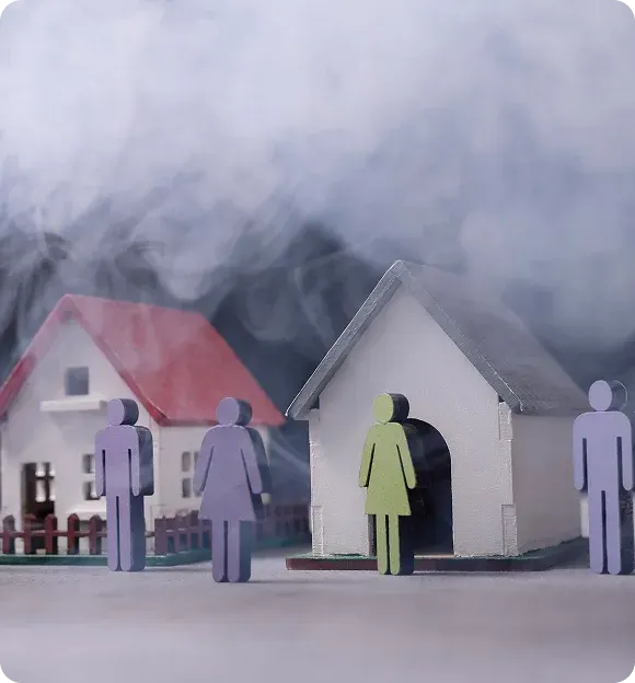 Miniature houses and colored paper cutout people surrounded by smoke symbolizing a natural disaster scenario.