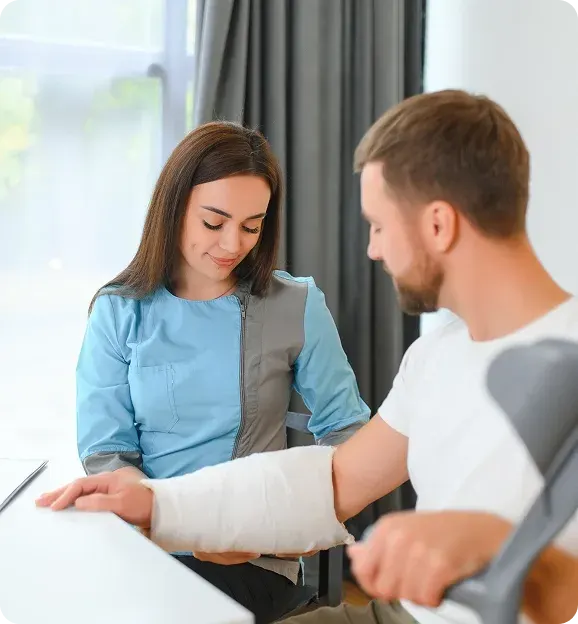 Female healthcare professional in blue scrubs gently holding a man's casted arm in a medical setting.