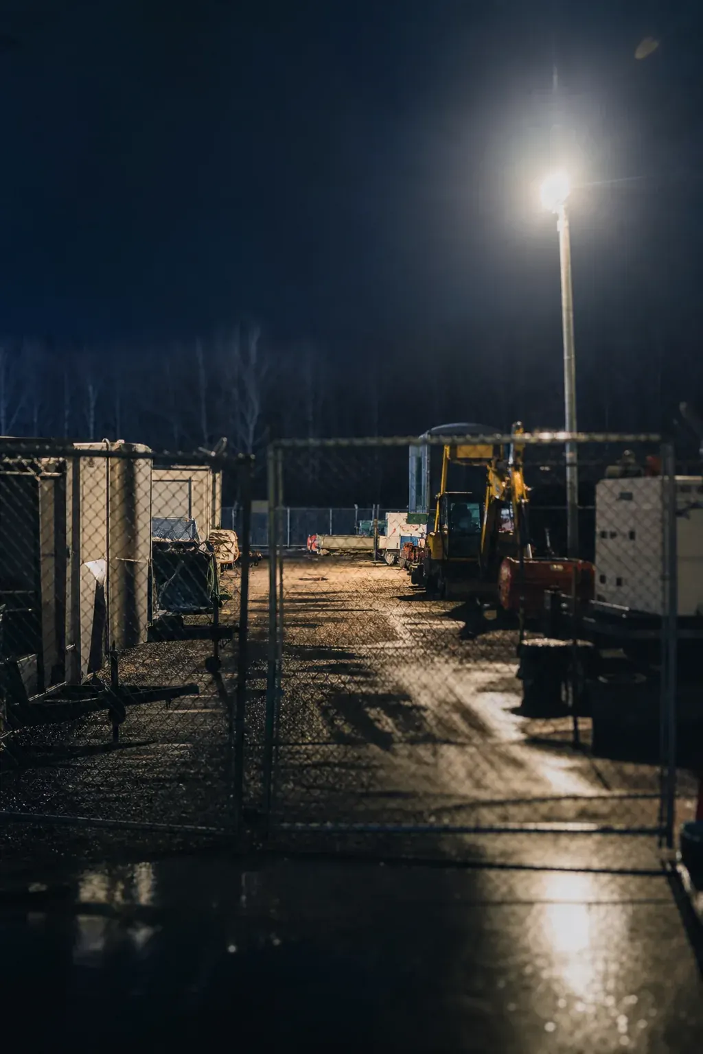 Contractor equipment secured in a fenced yard at night